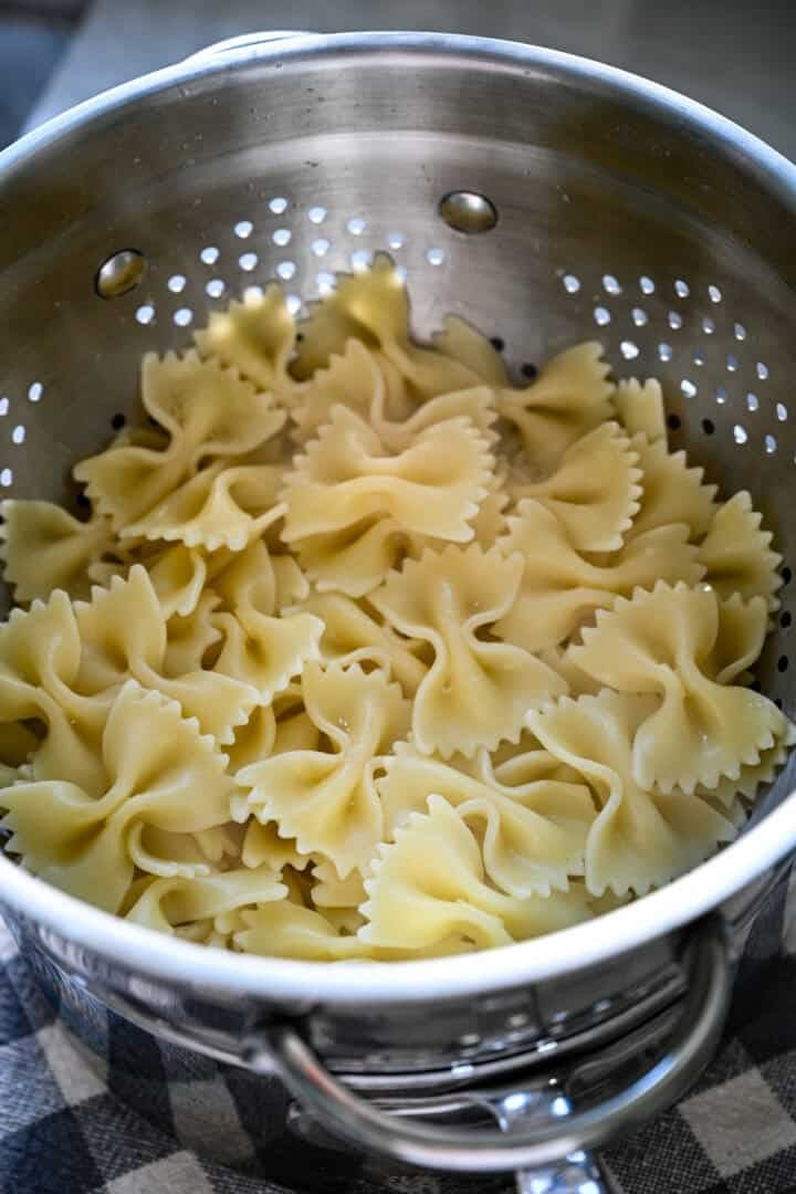 Ovanifrån av kokt fluga pasta som dräneras i ett metall durkslag i en kruka.