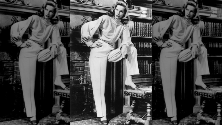 Lauren Bacall poserar nära en öppen spis i en Leah Rhodes turtleneck-tröja, avslappnade byxor och kilmulor i december 1946
