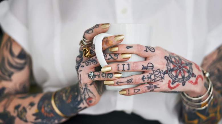En person med tatuerade händer och knogar som håller i en mugg