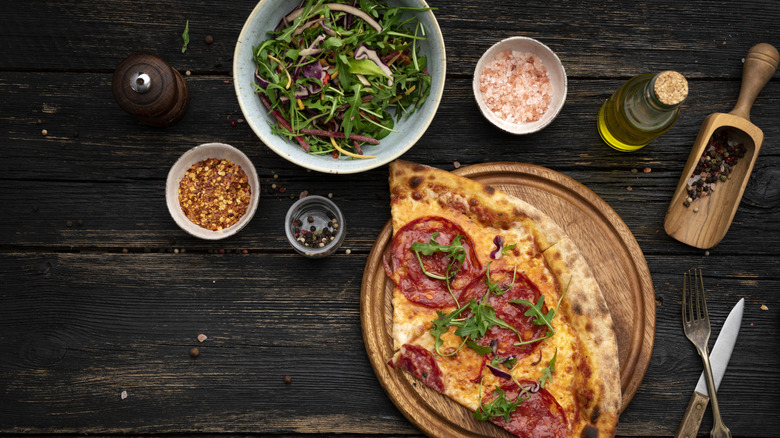 Pizza bredvid sallad och andra ingredienser