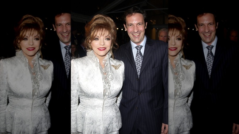 Joan Collins klädd i en vit kjolkostym bredvid Percy Gibson i kostym