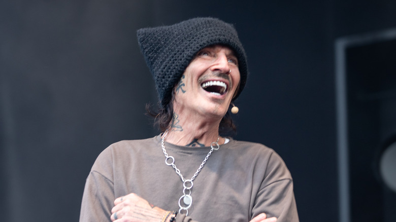 Tommy Lee skrattar på scenen iförd stickad mössa och långärmad t-shirt