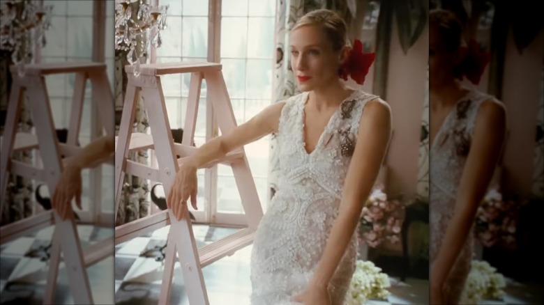 Sarah Jessica Parker som Carrie Bradshaw klädd i en bröllopsklänning med spetsfisksvans med en röd blomma i håret.